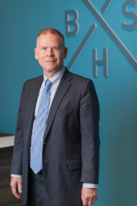 John Overton Belcher is posing with the Belcher Sykes Harrington wall sign.